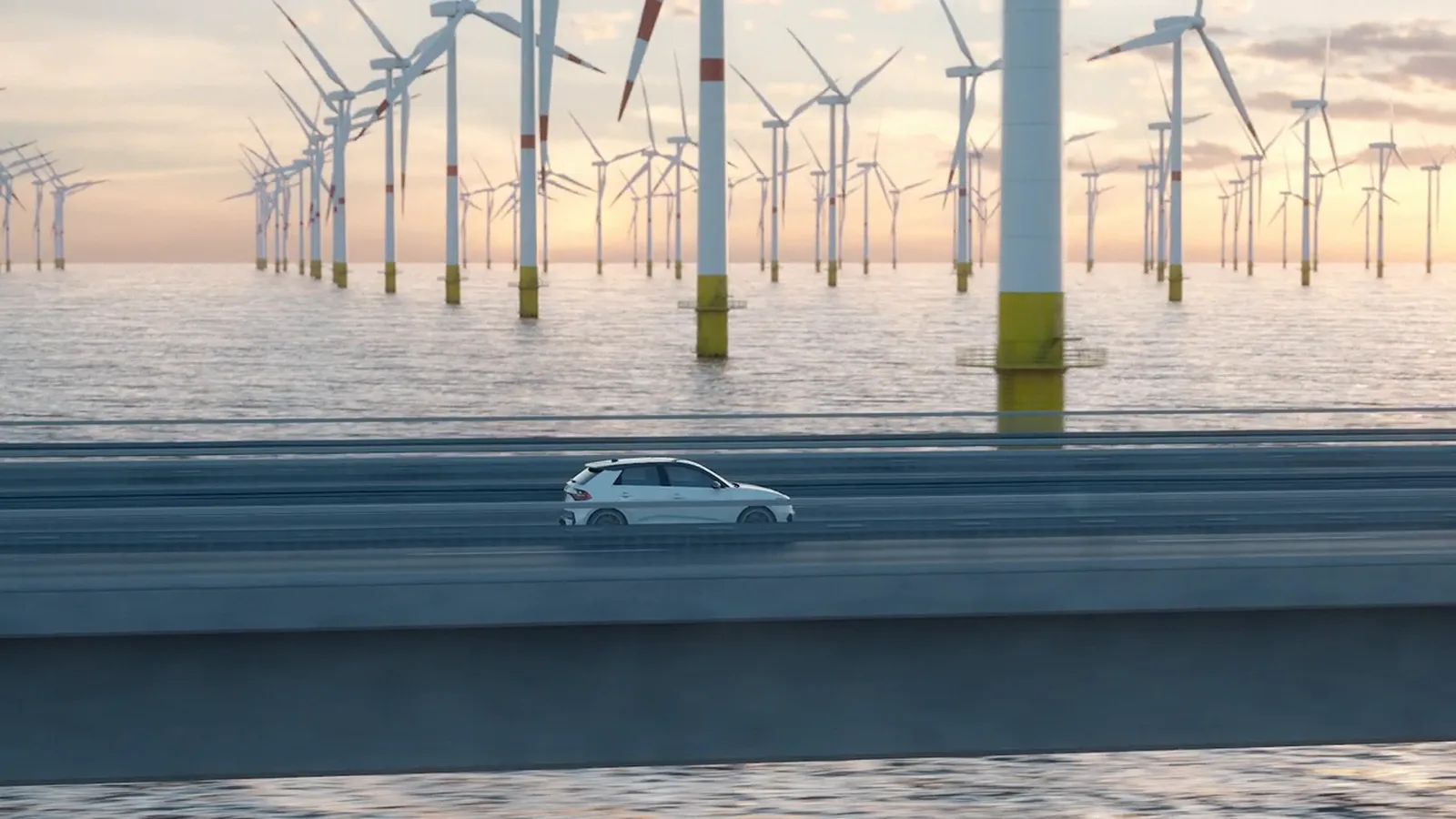 Weißes Elektroauto fährt über eine Küstenstraße, dahinter ein Offshore-Windpark