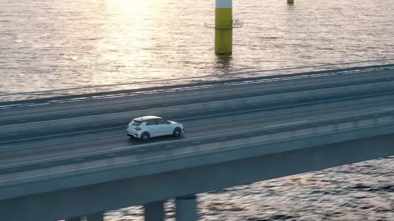 Weißes Elektroauto fährt über eine Küstenstraße, dahinter ein Offshore-Windpark